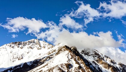 Snowy mountain peaks under a vibrant blue sky, with wispy clouds