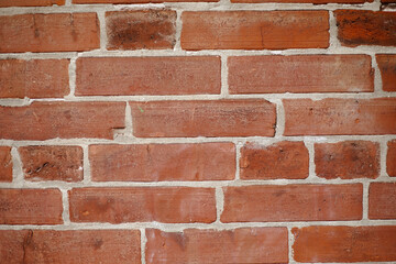 A close-up view of a classic red brick wall, showcasing a uniform pattern and varied texture. The bricks display natural color variations and imperfections, offering a rustic charm. 