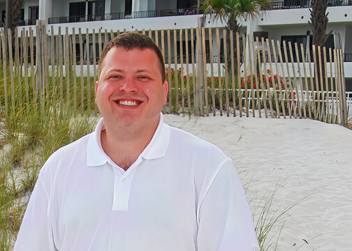 Smiling Man on Sandy Beach with Dune Fence and Resort in Background