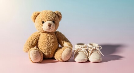 A teddy bear sits next to baby shoes on a pink surface with a blue gradient background.