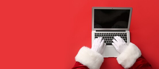 Santa Claus hands with modern laptop on red background with space for text
