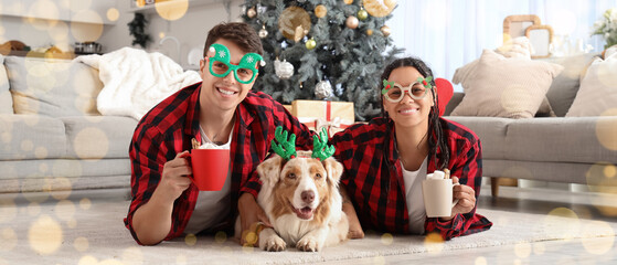 Happy young couple with cups of cocoa and dog lying at home on Christmas eve