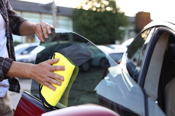 Man wiping car side window with yellow microfiber rag outdoors, closeup