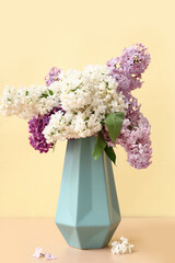 Beautiful bouquet of lilac flowers in vase on pale yellow background