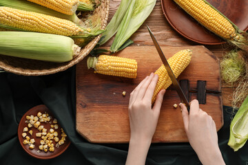 Woman cutting fresh corn cobs on wooden table