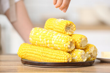 Woman salting boiled corn cobs on wooden table in kitchen