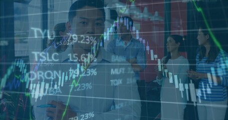 Writing Asian man creating financial graphs on glass board in office, with stock chart overlays