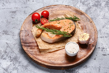 Plate of tasty salmon steak with tomatoes and garlic on grey background