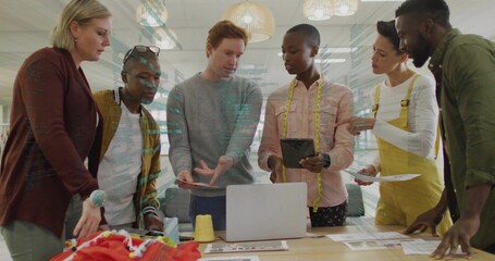 Collaborating group of designers leaning around table in design studio with laptop, measuring tape