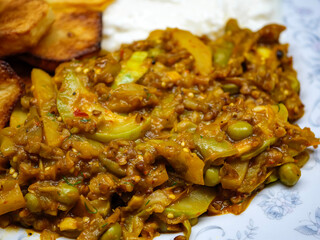 A close up photograph of a delicious homemade style Indian vegetable curry with fried potatoes featuring eggplant snake gourd and peas in a savory gravy
