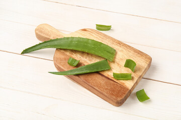 Cutting board with aloe vera leaves on white wooden background