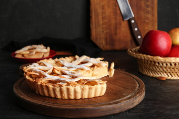 Wooden board with delicious apple pie on black background
