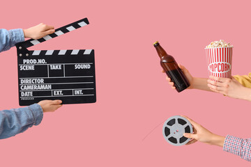 Hands with movie clapper, bucket of popcorn and beer on pink background