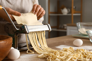 Young woman making pasta with machine at table in kitchen, closeup