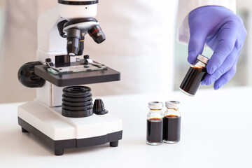 Male scientist with ampules and microscope on table in laboratory, closeup