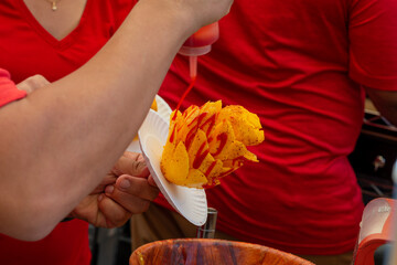 Mexican mango flower or mango on a stick being made by a street vendor at a market. The fruit is...