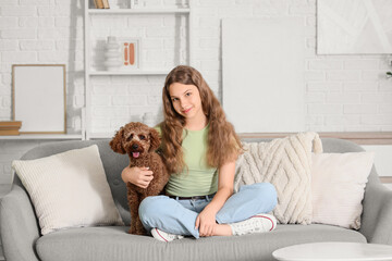 Teenage girl with Poodle dog sitting on sofa at home