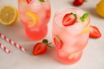 Glasses of drink with ice cubes, strawberry and lemon slices on white background