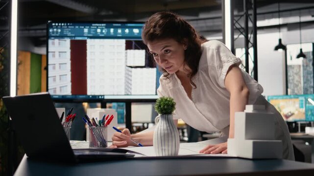 Woman real estate engineer reviews city planning blueprints on laptop, setting infrastructure goals on sustainability while preparing a pitch on residential project urban development. Camera A.