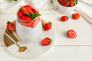 Glass of tasty chia seed pudding with fresh strawberries and mint on white wooden background