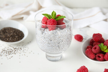 Glass of tasty chia seed pudding with fresh raspberries and mint on white background