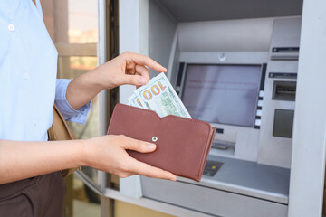 Businesswoman putting dollar banknotes into wallet near ATM, closeup