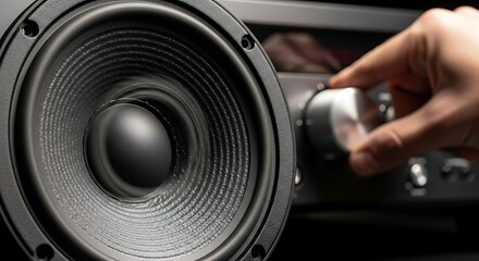 Close up of a black speaker with a hand turning a knob on an audio receiver in the background