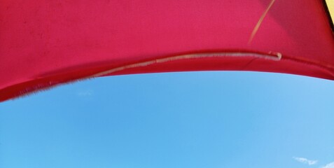 A bright red umbrella against a clear blue sky on a sunny day.