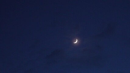 A bright crescent moon hangs in a deep blue twilight sky, with a single star visible above, creating a serene and timeless celestial scene. - Powered by Adobe