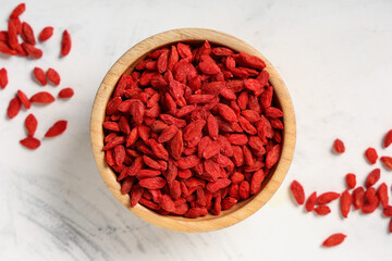 Wooden bowl with red dried goji berries on white background