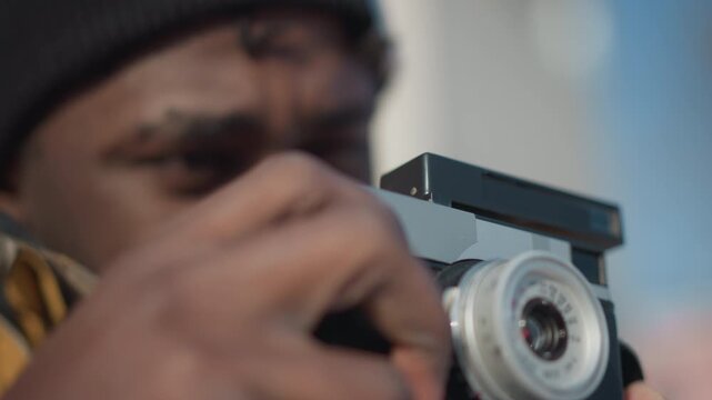 close up of hands of photo enthusiast handling vintage camera, fingers delicately turning focus ring to adjust lens under soft sunlight, snowy urban background creating cinematic vibe