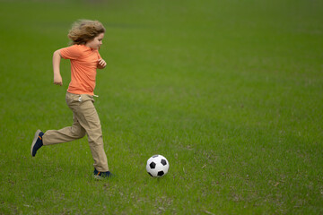 Obraz premium Kid playing football in the park. Child kicking a football ball on field. Happy boy running with a football ball. Children playing soccer outdoors. Kid play football on the grass. Summer soccer game.