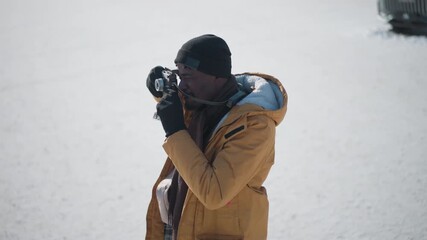 high angle view of photographer peering through viewfinder gloved hands adjusting focus dial then surveying urban winter landscape under bright sunshine clear sky capturing textured crisp snow