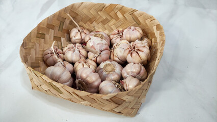 Fresh garlic bulbs in a traditional woven bamboo basket on a white background. Ideal for culinary design, healthy food themes, spice concepts, and agriculture content.