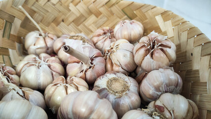 Fresh garlic bulbs in a traditional woven bamboo basket on a white background. Ideal for culinary design, healthy food themes, spice concepts, and agriculture content.