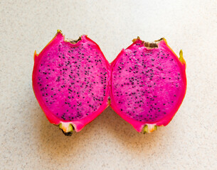 A fresh dragon fruit cut in half, showing its bright pink flesh with many tiny black seeds.