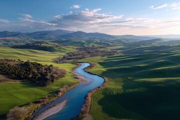 Aerial perspective of rolling hills and a winding river under a bright, partly cloudy sky during