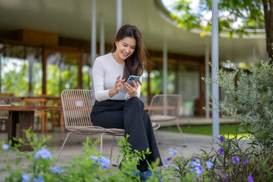 Businesswoman using smartphone in outdoor cafe, enjoying modern architecture and nature