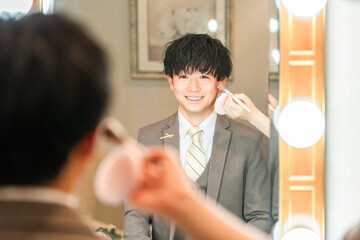 結婚式場のブライズルームでメイクをするスーツ,タキシード姿の新郎
