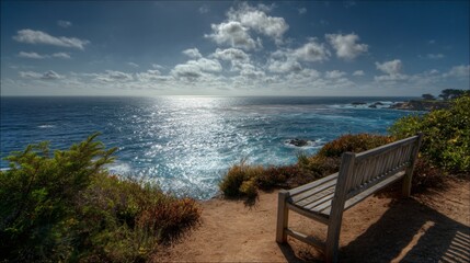 Obraz premium Scenic coastal view with wooden bench overlooking sparkling blue ocean under sunny sky.