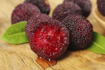 Fresh Bayberries on Wood Surface - Exotic Red Fruit with Green Leaves