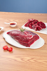 Fresh Raw Beef Steaks on Wooden Cutting Board with Herbs and Tomatoes Ready for Cooking