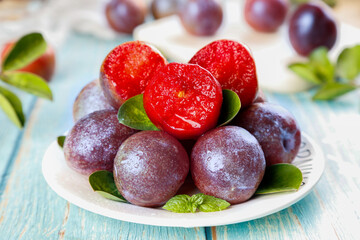 Freshly picked red plums in row with heart-shaped cut showing flesh on wooden table