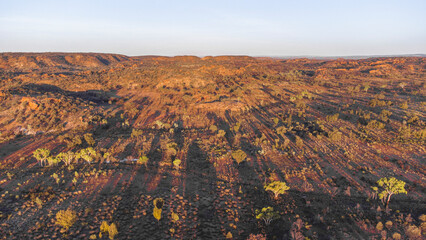 This aerial shot captures the golden hour illuminating a vast, rugged landscape. Rolling...