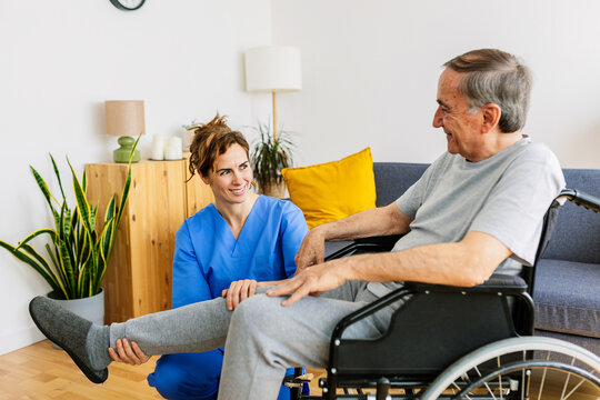 Smiling nurse assisting a happy senior man in a wheelchair with leg exercises in a home healthcare setting