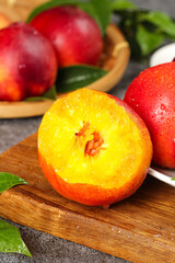 Fresh Red-Skinned Nectarine Cut in Half Showing Yellow Center on Wooden Board