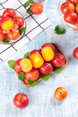 Fresh Red Plums from Guangdong in Wooden Bowl with Mint Leaves on White Rustic Background