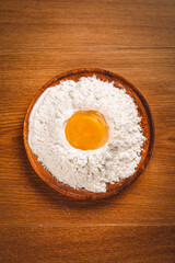 Fresh wheat flour with egg yolk in wooden bowl ready for baking homemade bread dough
