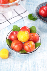 Fresh Red and Yellow Plums with Mint Leaves in Bowl on Rustic Wooden Background
