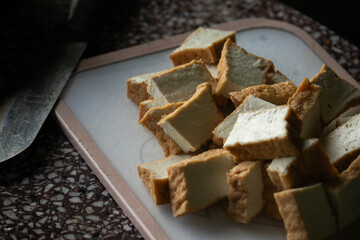 Cubes of golden fried tofu on a cutting board, next to a knife. A scene of preparing a vegetarian meal at home.